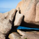 riesige bizarre Felsformation vor blauem Meer, das man in Lücken durchscheinen sieht.